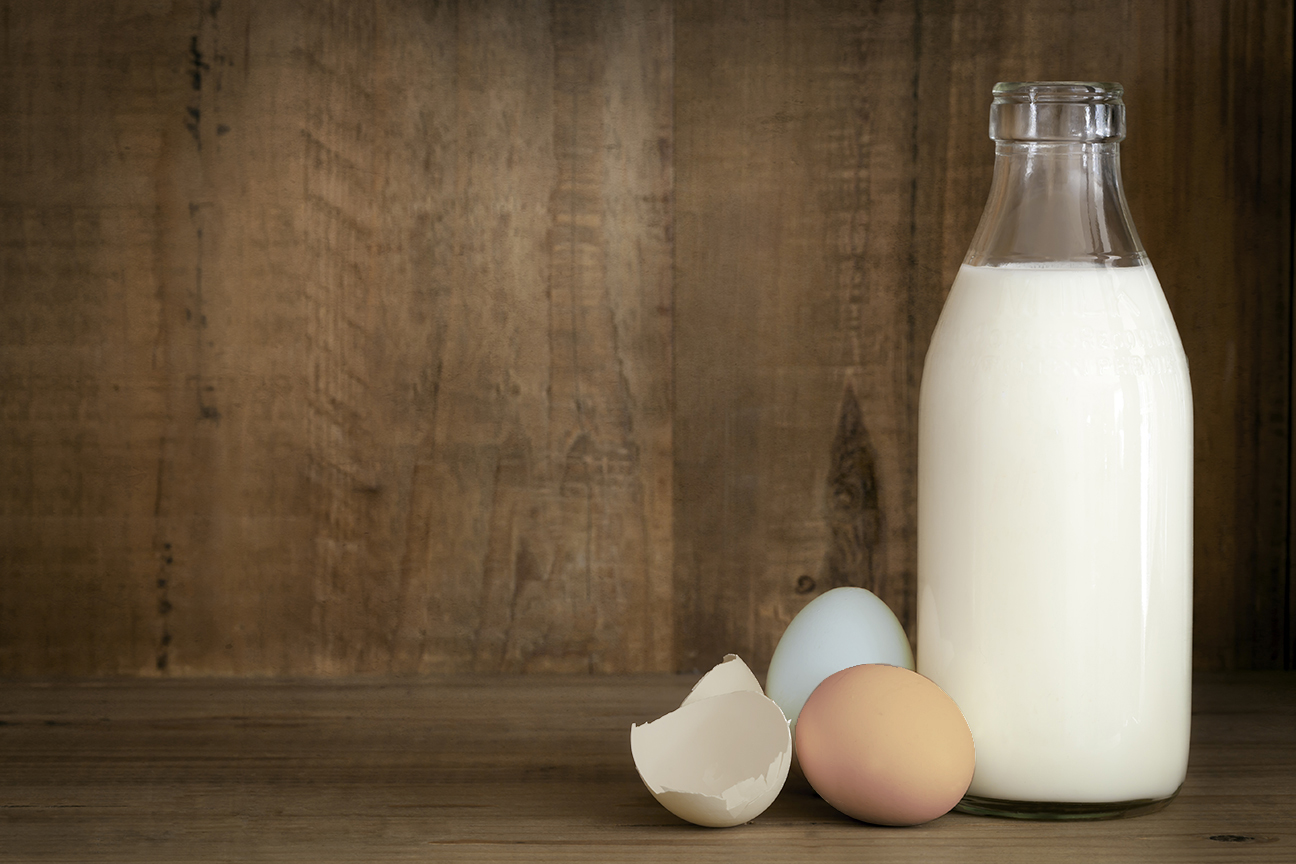 Bottle of milk alongside fresh eggs and an eggshell on a wooden surface, highlighting natural ingredients for cooking and baking.